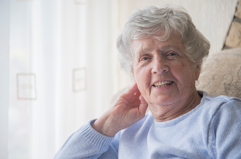 Senior Caucasian woman sitting indoors in chair smiling at camera in Sunbury Gardens
