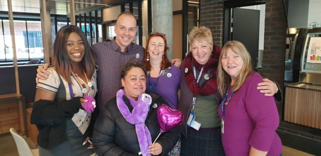 Six people smiling at the camera and wearing purple